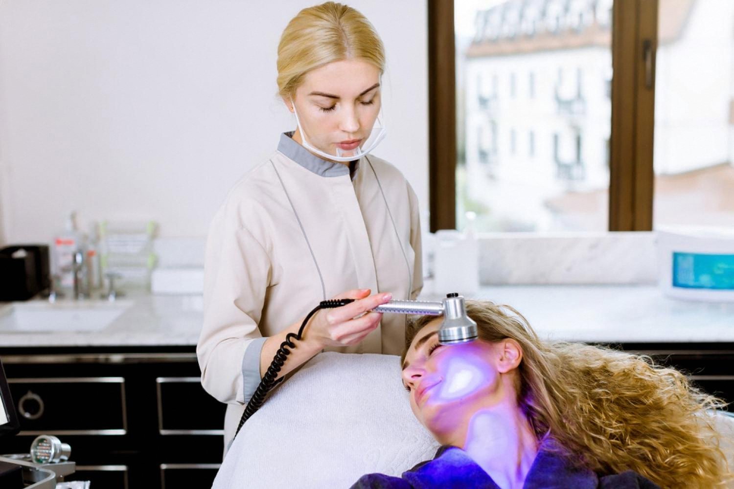 Young woman receiving a laser facial treatment on her cheek at an aesthetic clinic