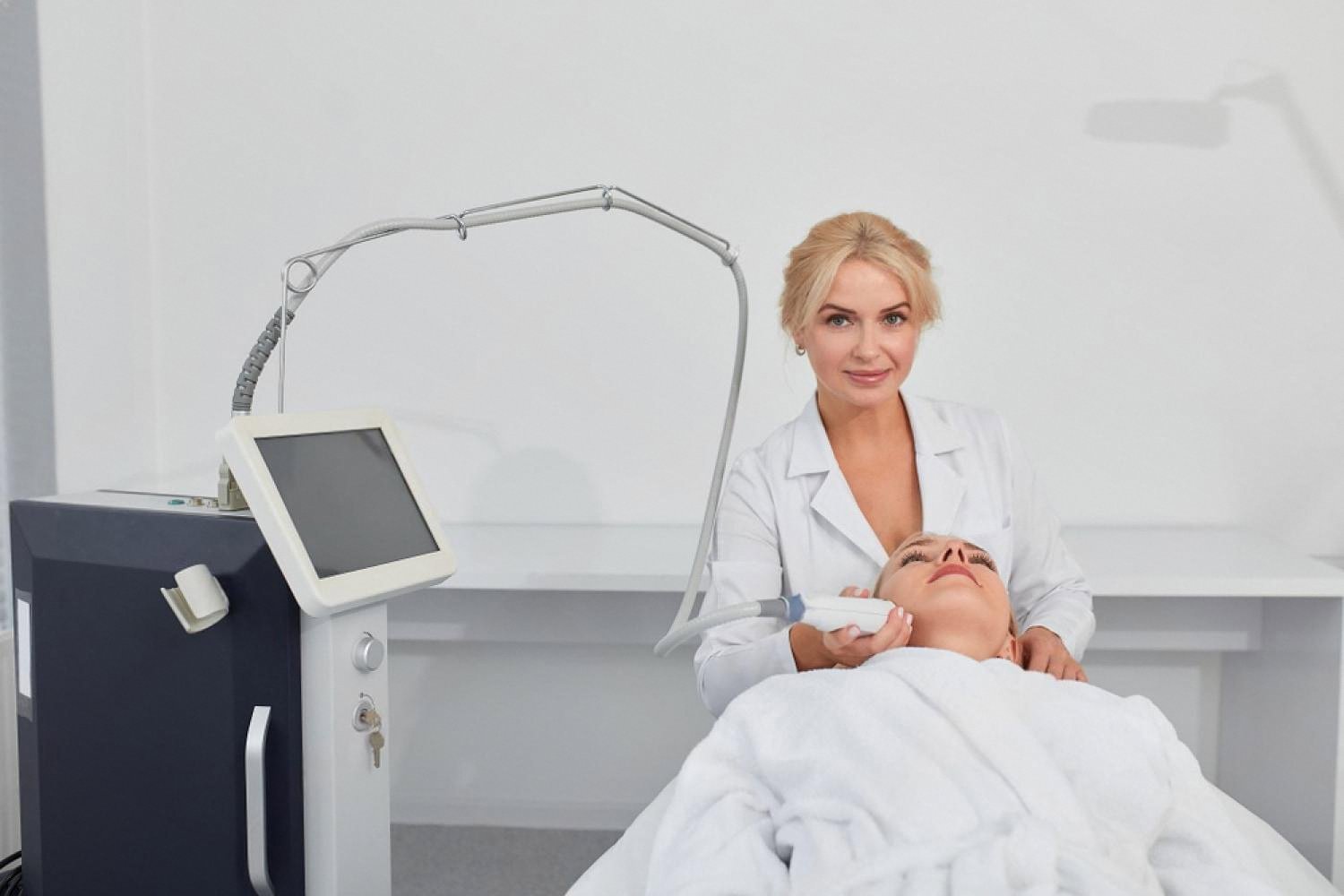 Aesthetician performing laser photorejuvenation on a client lying on a treatment bed